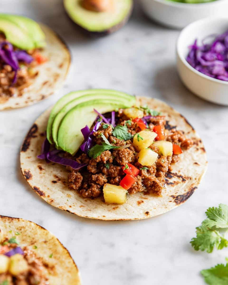 A small white corn tortilla with a lightly charred texture serves as the bottom layer. On top, there is a layer of cooked ground meat mixed with small yellow chunks that look like pineapple, and diced red bell peppers adding bright spots of color. To the side, thin slices of green avocado are carefully placed, slightly fanned out. Small pieces of purple cabbage and green cilantro leaves are scattered on top and around, adding fresh color contrasts. The background is a white marbled texture with some blurred white bowls and half an avocado nearby. Photo taken with an iphone --ar 4:5 --v 7