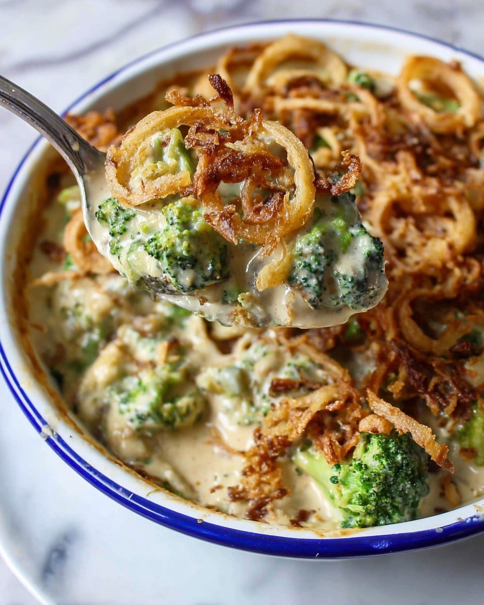 The image shows a close-up of a dish with three main layers: the base is creamy and light beige with a thick sauce texture, mixed with bright green broccoli florets that add a fresh pop of color. On top of this creamy layer, there are rings of crispy, golden-brown fried onions scattered evenly, adding a crunchy texture. The dish is served in a white plate with a thin blue rim, set against a white marbled surface. A silver spoon holds a scoop of the dish, showcasing a dense combination of the creamy sauce, green broccoli, and crispy fried onions. Photo taken with an iphone --ar 4:5 --v 7
