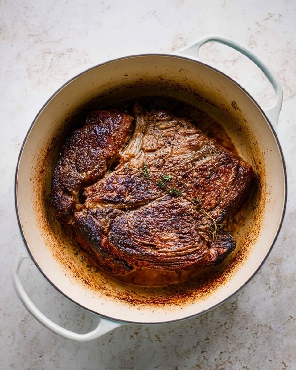 A large piece of browned meat with dark, crispy edges and visible muscle texture sits in an oval white pot with two handles, the inner surface of the pot showing light browning from cooking. The meat’s surface is uneven with a mix of darker and lighter brown areas and is placed flat in the center of the pot. The pot rests on a white marbled surface, adding a clean and bright background contrast. Photo taken with an iphone --ar 4:5 --v 7