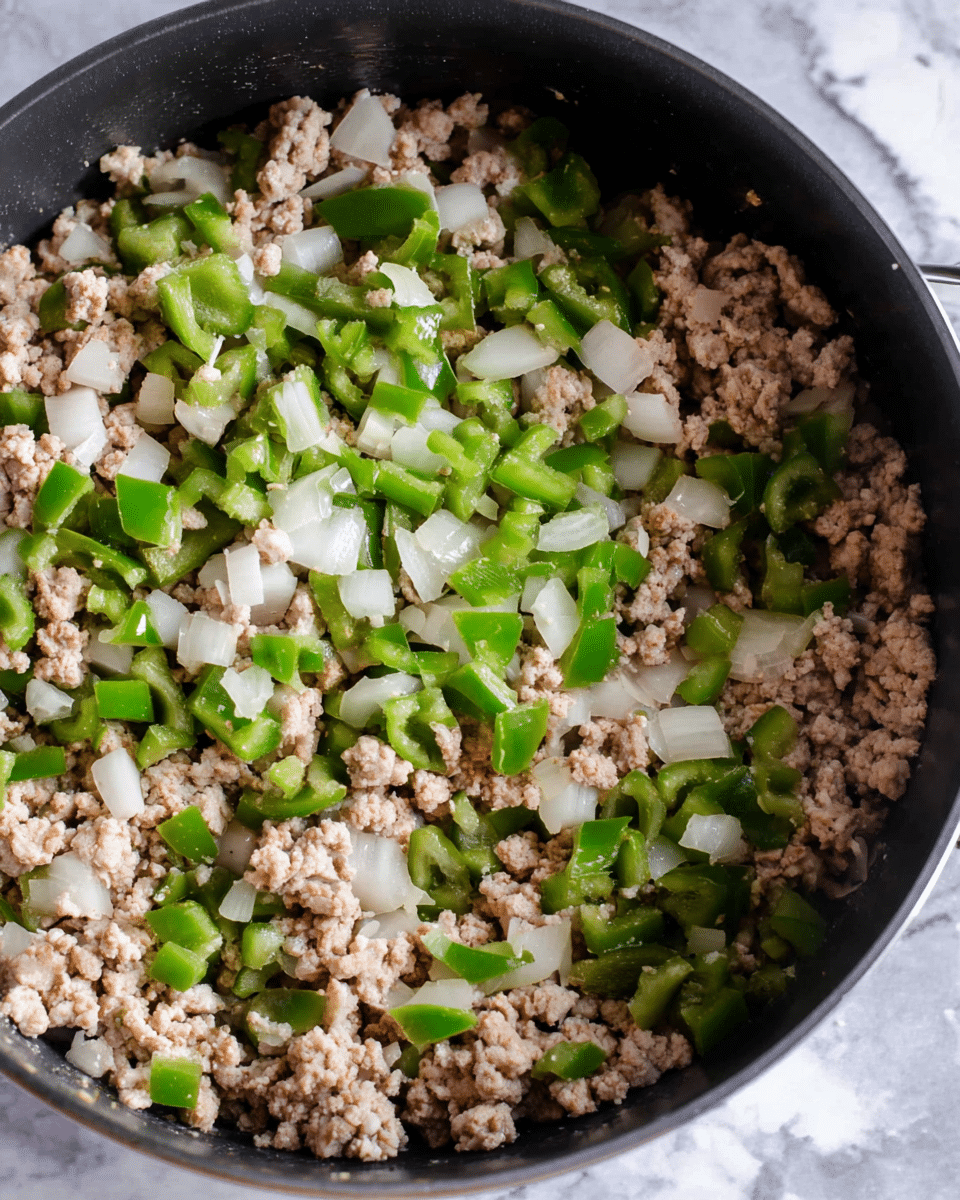 A close-up top view of a black cooking pot filled with three main layers: the bottom layer of small, light beige cooked ground meat crumbles, mixed throughout with bright white chopped onion pieces, and vibrant green chopped bell pepper chunks scattered evenly in the pot. The textures show the soft meat with some graininess, firm onion pieces, and fresh, slightly shiny bell peppers. The pot rests on a surface with a white marbled texture. photo taken with an iphone --ar 4:5 --v 7