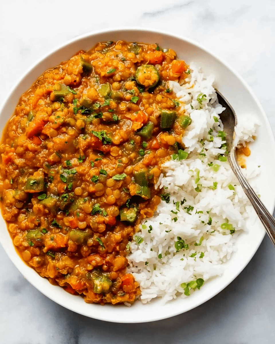 The image shows one white plate with two layers: on the left, a thick stew made of orange lentils mixed with diced green okra, small bits of orange carrots, and green herbs sprinkled on top, creating a chunky textured layer; on the right, a fluffy layer of plain white rice partially mixed into the stew, with a few green herb pieces scattered on it. A silver spoon is placed on the bottom right edge of the plate, partially touching the rice. The plate is set on a white marbled surface. photo taken with an iphone --ar 4:5 --v 7