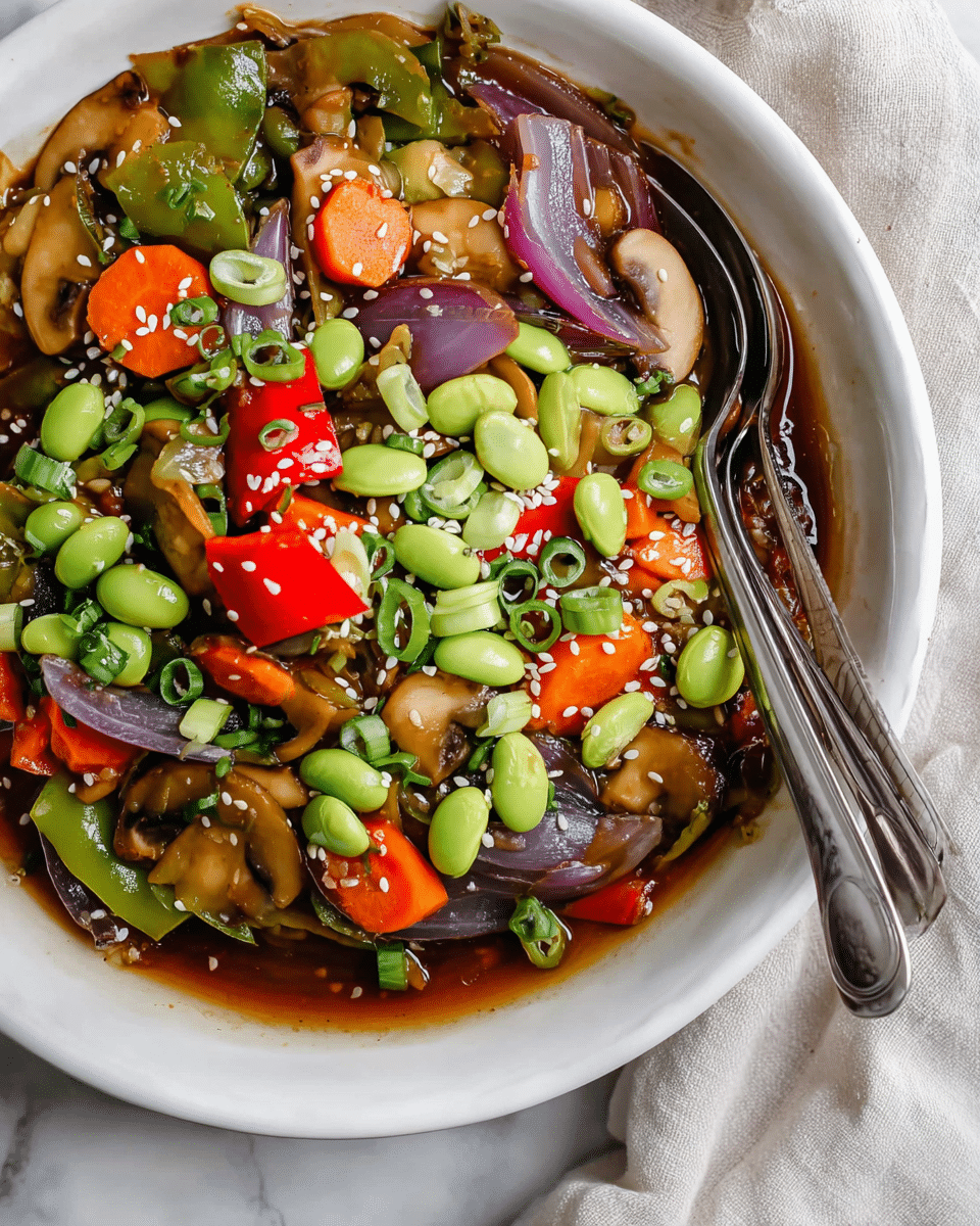 This image shows a white bowl filled with a colorful vegetable stir fry. The bottom layer has a glossy brown sauce with sliced mushrooms and carrot rounds. On top, there are chunks of green bell pepper and red bell pepper pieces, along with thick slices of cooked purple onion. Scattered over the vegetables are bright green edamame beans and thinly sliced green onions. Small white and black sesame seeds are sprinkled around the dish. Two silver spoons rest inside the bowl on the right side, partly submerged in the sauce. The bowl sits on a white marbled surface with a light-colored cloth partially visible on the right side. Photo taken with an iphone --ar 4:5 --v 7