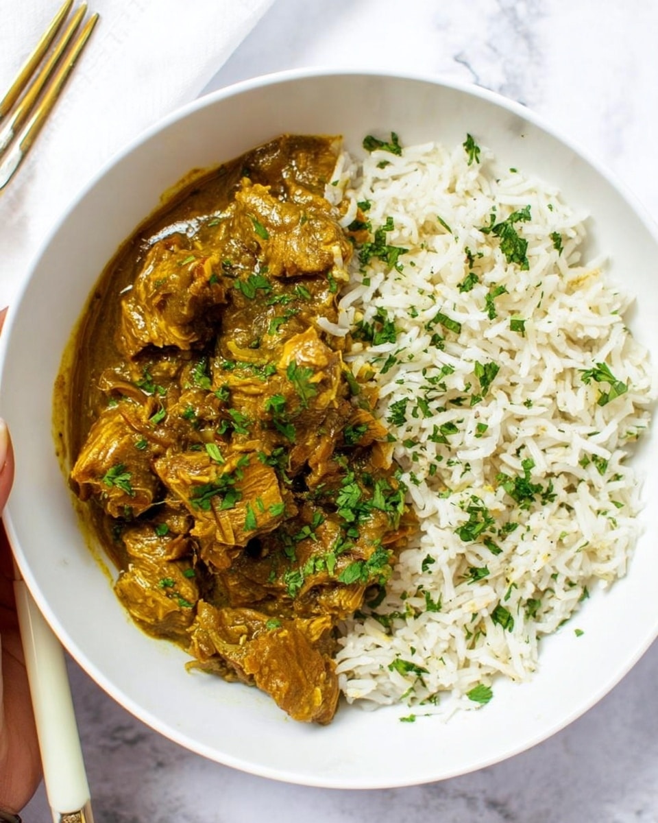 A white bowl on a white marbled surface holds two main layers: a generous portion of light, fluffy white rice with some green herb pieces on the right side, and a rich, golden brown curry with tender chunks of meat covered in a thick sauce on the left. The curry is sprinkled with fresh chopped green herbs, adding a bright contrast to the dish. The bowl edges are smooth and the food looks warm and inviting. In the top left corner, a woman's hand is holding a fork with a cream-colored handle. Photo taken with an iphone --ar 4:5 --v 7