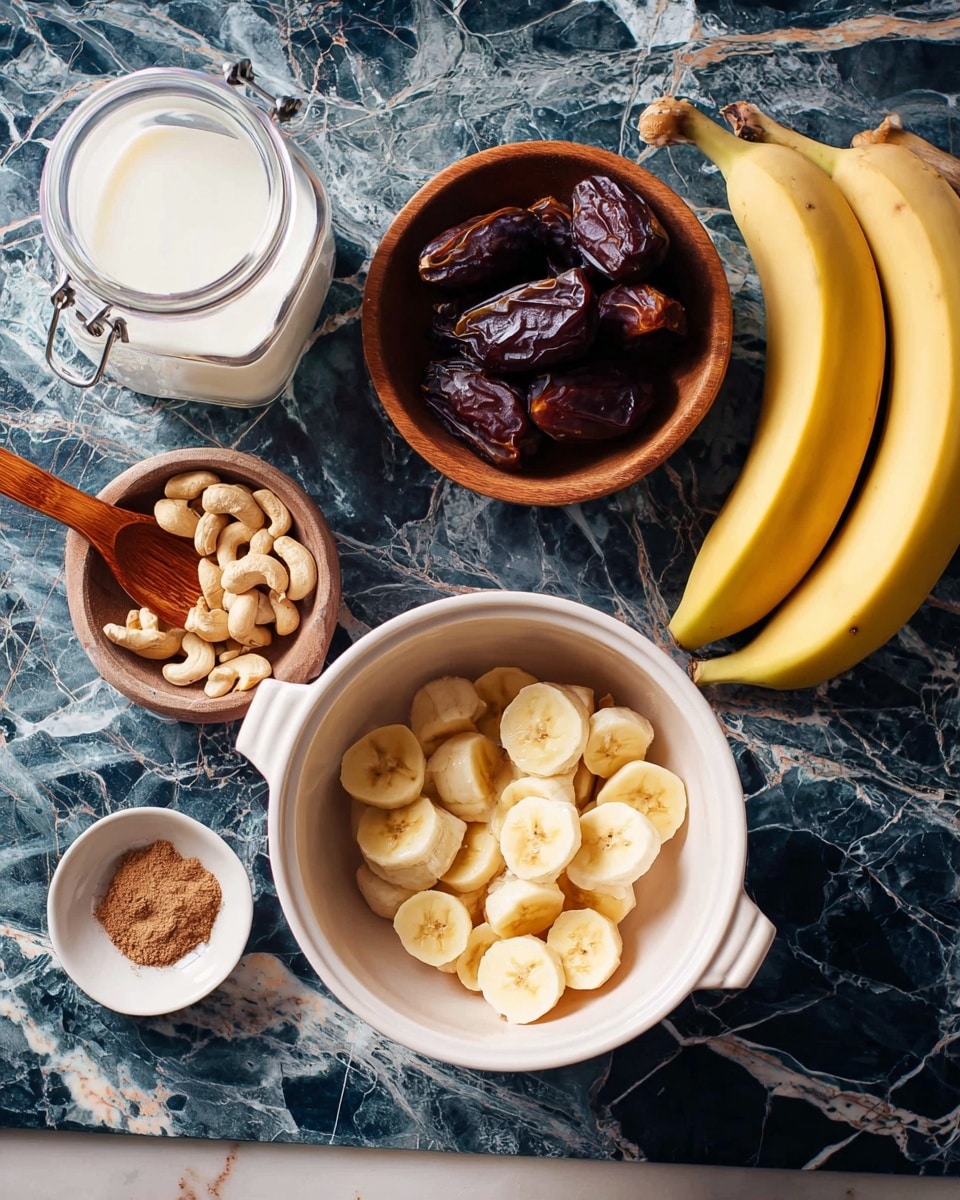 The image shows a white bowl with two handles filled with light yellow banana slices, placed on a table with a dark blue and white marbled texture. Nearby, there is a white small bowl holding several dark brown dates, and a brown wooden bowl filled with cashew nuts. A small white dish contains brown cinnamon powder next to the wooden bowl. A glass jar of white milk and a small white container of brown powder with a wooden spoon are also on the table. Two whole yellow bananas rest on the right side of the setting. photo taken with an iphone --ar 4:5 --v 7