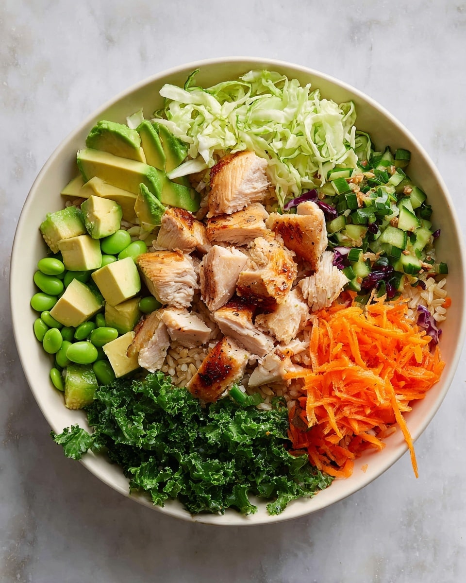 A white bowl filled with a colorful mix of fresh ingredients arranged in layers. At the center, there are pieces of cooked chicken with a light brown grilled texture. Surrounding the chicken are small cubes of bright green avocado scattered on one side. Light green chopped cabbage sits behind the avocado. Light brown cooked rice forms a base layer underneath and around the chicken. Bright orange shredded carrots are placed on both sides of the bowl along with diced dark green kale and chopped cucumber pieces in a medium green shade. On one side, there are also small bright green edamame beans mixed with chopped herbs. All elements rest on a white marbled surface. Photo taken with an iphone --ar 4:5 --v 7