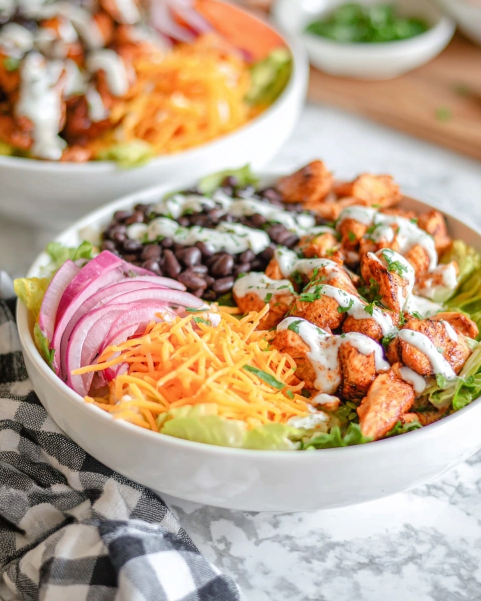 A white bowl holds a colorful layered salad with five visible layers: at the bottom, a bed of green lettuce, topped with bright orange shredded cheese spread across the bowl. On one side, there are black beans drizzled with a creamy white sauce and sprinkled with chopped green herbs. Next to the beans are pieces of cooked orange chicken with a light drizzle of white sauce. Thinly sliced pink onions and orange shredded carrots are scattered on top, adding more color and texture. The bowl is placed on a white marbled surface with a checkered cloth nearby. In the background, there is a second similar white bowl slightly out of focus. Photo taken with an iphone --ar 4:5 --v 7