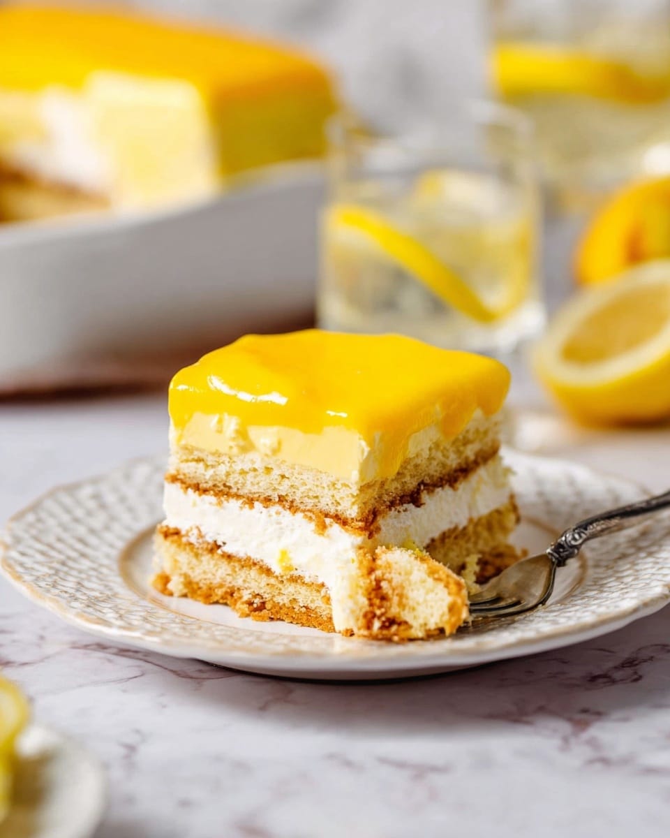 The image shows a square slice of layered cake on a white plate with a textured edge, placed on a white marbled surface. The cake has three visible layers: a bottom light brown sponge layer, a middle creamy white layer, and a top bright yellow smooth layer that looks like a thick glaze or custard. A fork with a piece of cake is placed on the right side of the plate, near the slice. In the background, there is a white dish with more cake and blurred lemon wedges and glasses, adding a fresh look. The lighting highlights the soft texture of the cake layers and the shiny smoothness of the yellow topping photo taken with an iphone --ar 4:5 --v 7