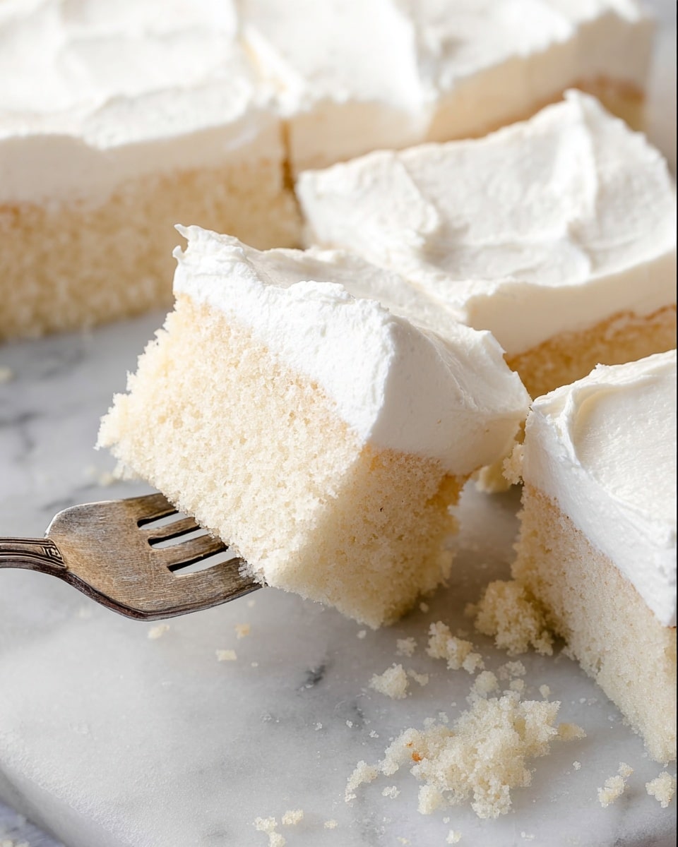 The image shows several square pieces of white cake with a thick layer of smooth white frosting on top. One piece is taken on a silver fork, showing the light and soft texture inside the cake. The pieces are placed on a white marble surface with some crumbs around them, giving a fresh and clean look. The frosting looks creamy and evenly spread over each piece, with a bit of a wavy texture on top. photo taken with an iphone --ar 4:5 --v 7