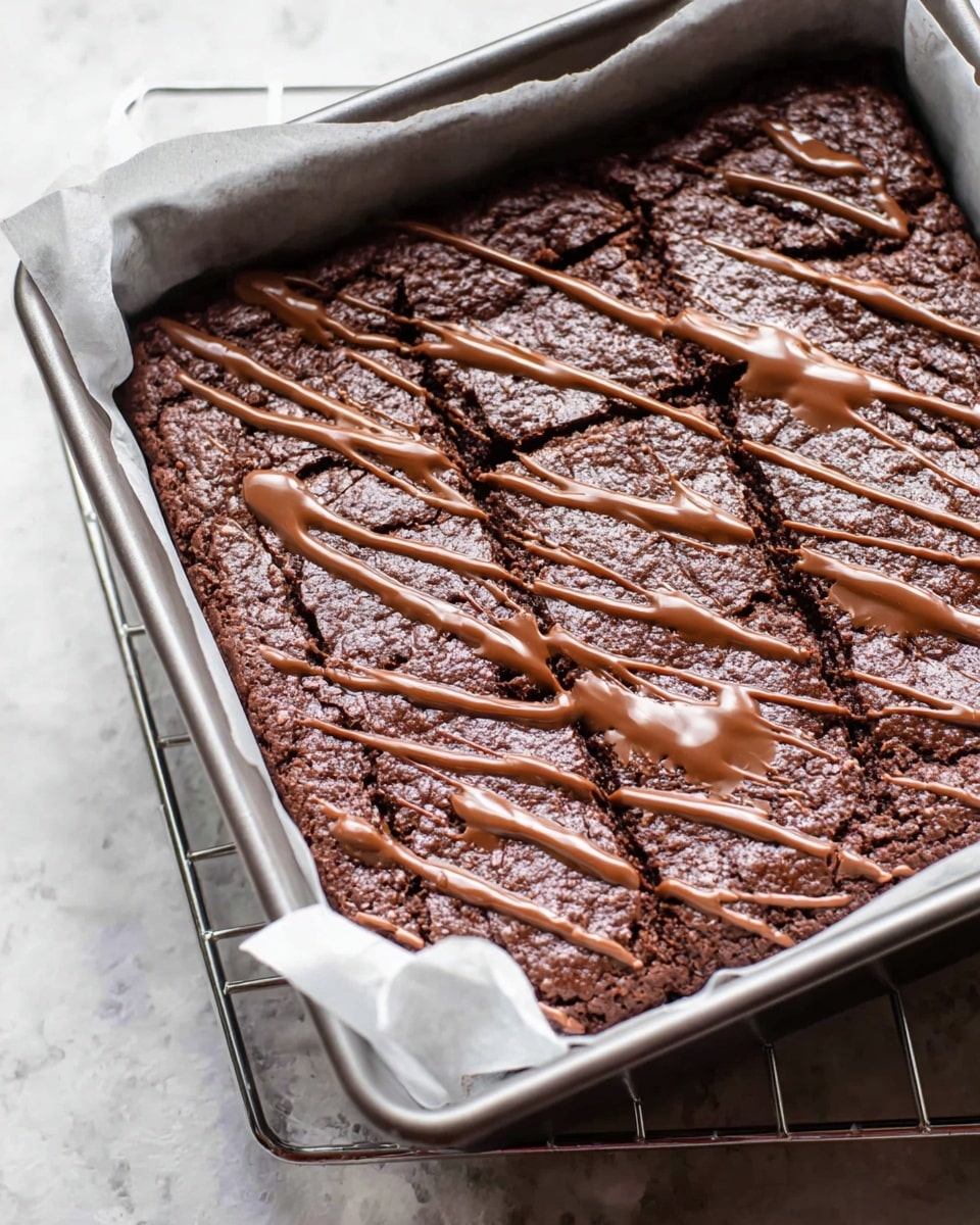 This image shows a single-layer dark brown chocolate brownie in a metal rectangular pan lined with white parchment paper. The brownie has a rough texture on top and is drizzled with smooth milk chocolate in thin and thick lines, creating a shiny pattern across the surface. The pan is placed on a rack, and the background is a white marbled texture. photo taken with an iphone --ar 4:5 --v 7