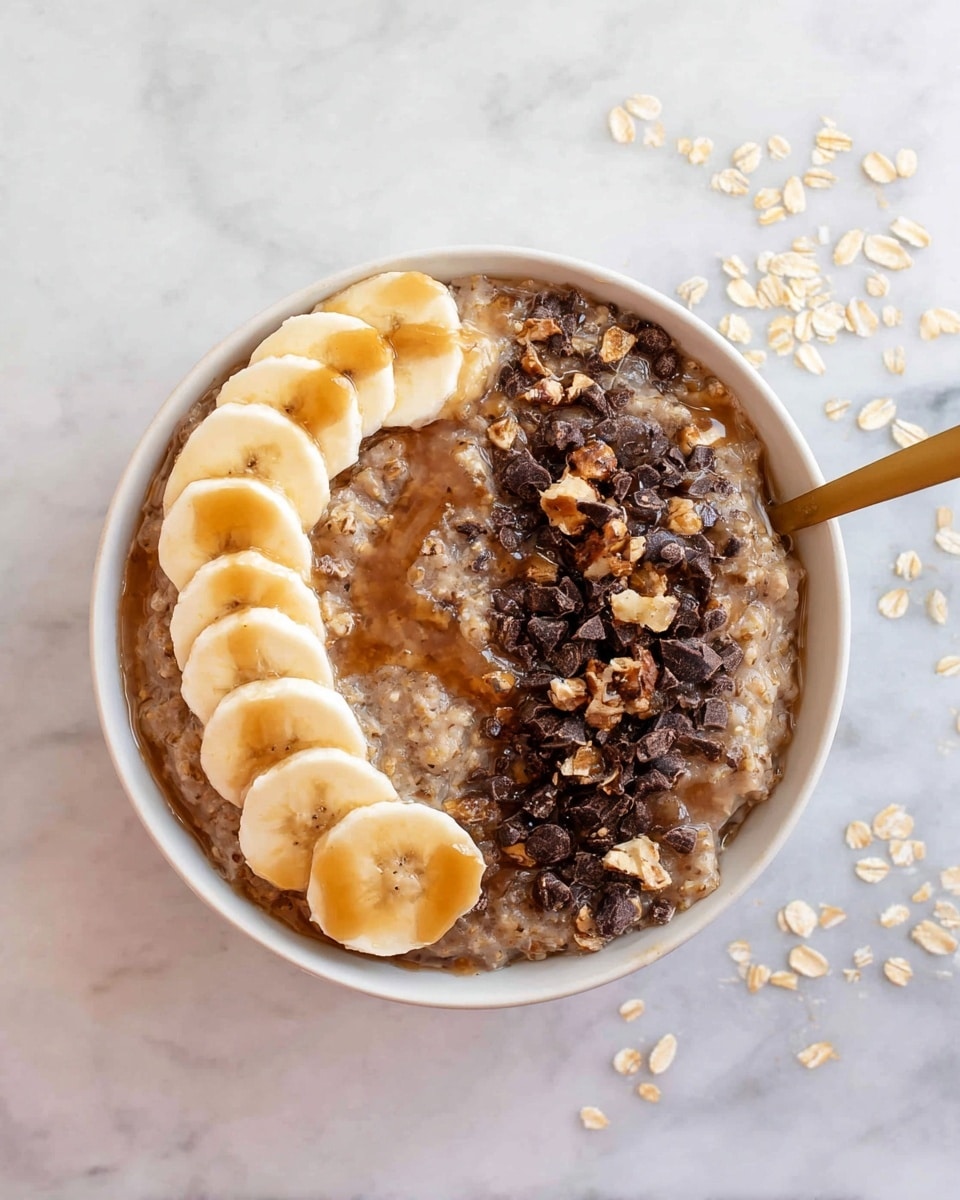 A white bowl sits on a white marbled surface, filled with oatmeal that has a soft, wet texture and light brown color. On one side, there is a neat row of banana slices, pale yellow with a smooth surface, drizzled with golden syrup. The rest of the oatmeal is topped with small dark brown chocolate chunks and tiny bits of chopped nuts, adding rough texture and contrast. A gold spoon is partially dipped into the oatmeal on the right side, shining against the food. Some oats are scattered around the bowl on the surface. photo taken with an iphone --ar 4:5 --v 7