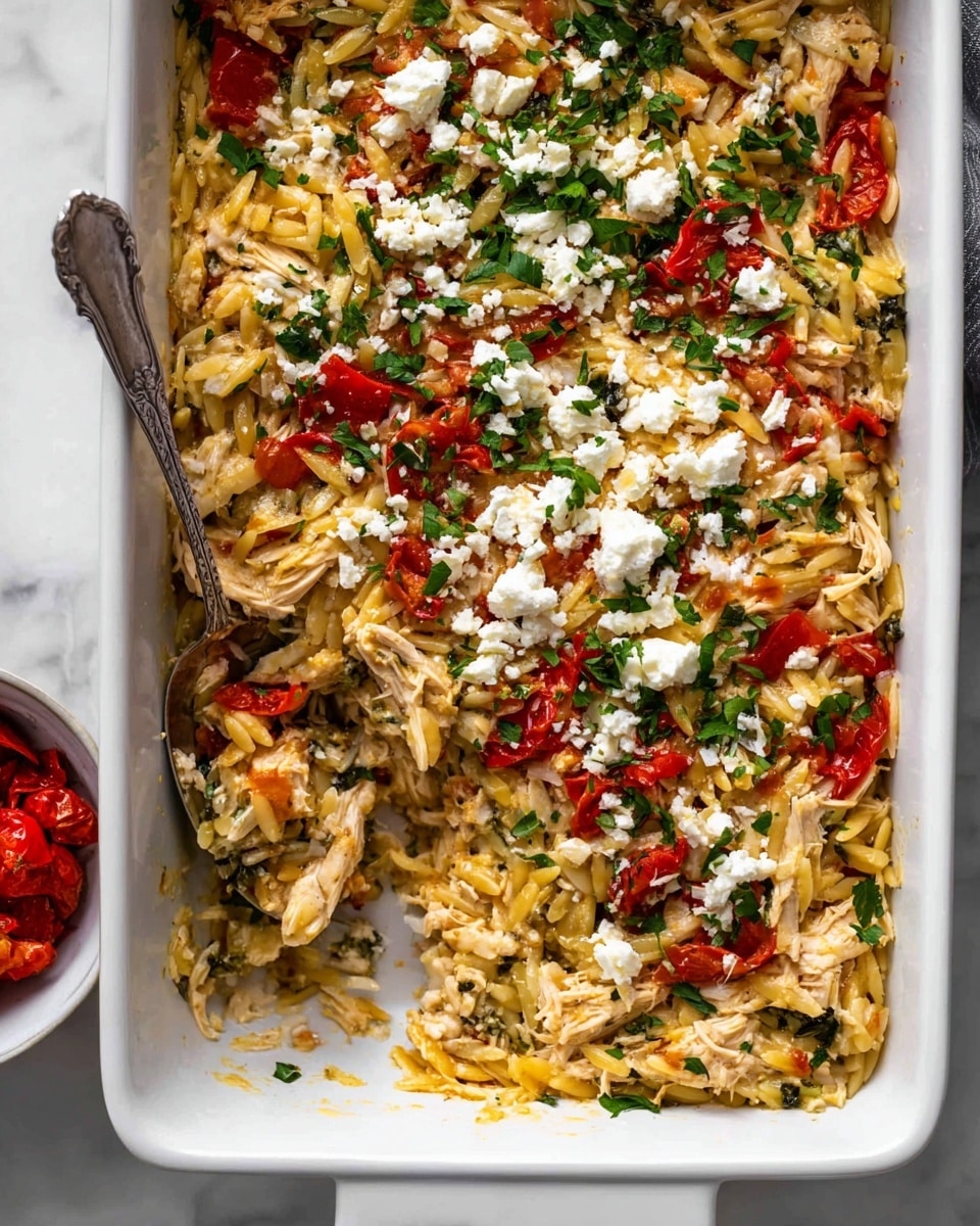 A white rectangular baking dish filled with a mixed pasta casserole showing about three layers: a base of shredded light-colored chicken and cooked orzo pasta, scattered pieces of red roasted peppers, and a topping of crumbled white cheese and chopped green herbs, with a spoon partially inserted into the dish revealing soft, moist textures. The dish rests on a white marbled surface, and a small white bowl holding red roasted peppers is visible in the lower left corner of the image. photo taken with an iphone --ar 4:5 --v 7