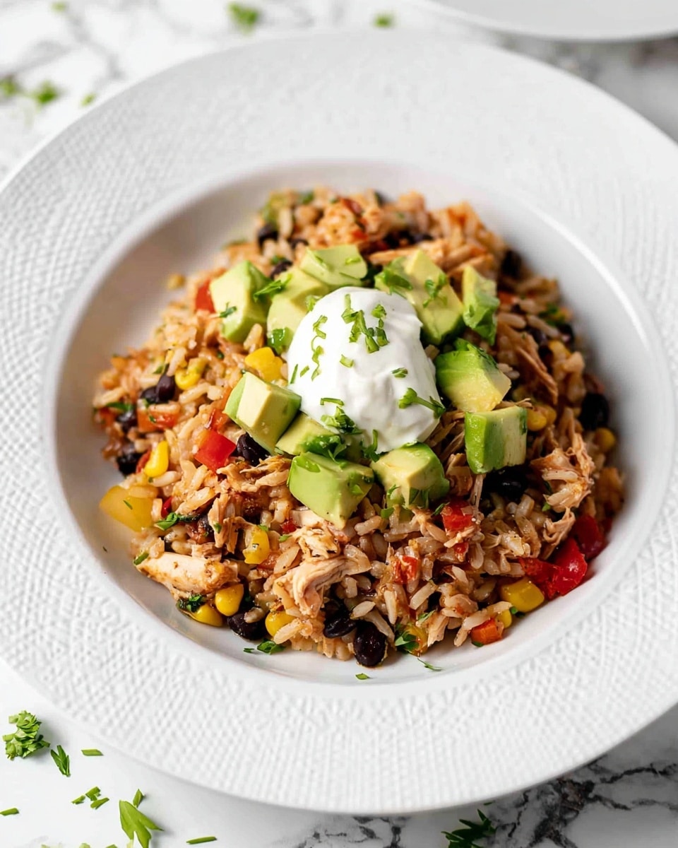 A white plate with a textured rim holds a colorful rice dish in the center. The base layer is light brown rice mixed with shredded chicken, black beans, small red and yellow bell pepper pieces, and corn kernels. On top of this are scattered chunks of green avocado and thin slices of green onion. A dollop of white creamy sauce sits neatly on the middle of the dish. The plate is set on a white marbled surface with a few small green herb pieces around the rice for garnish. photo taken with an iphone --ar 4:5 --v 7