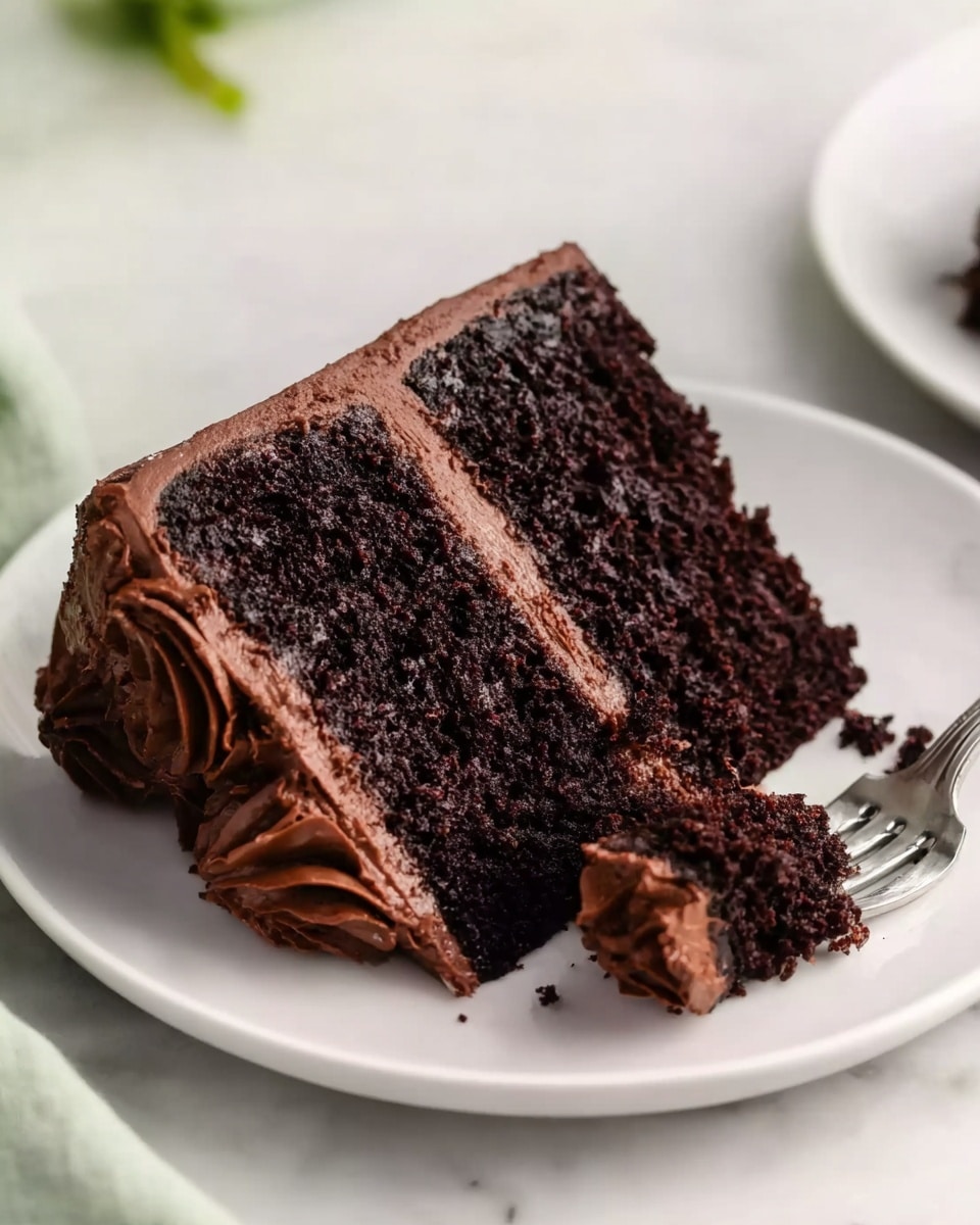 A slice of dark chocolate cake with two thick layers of moist, rich, almost black cake and a smooth, creamy medium brown chocolate frosting between the layers and covering the outside. The frosting has soft swirls and a slightly shiny texture. The slice is on a white plate on a white marbled surface, with a silver fork placed next to the slice, holding a small piece of the cake. A woman's hand is about to pick up the fork. Photo taken with an iphone --ar 4:5 --v 7