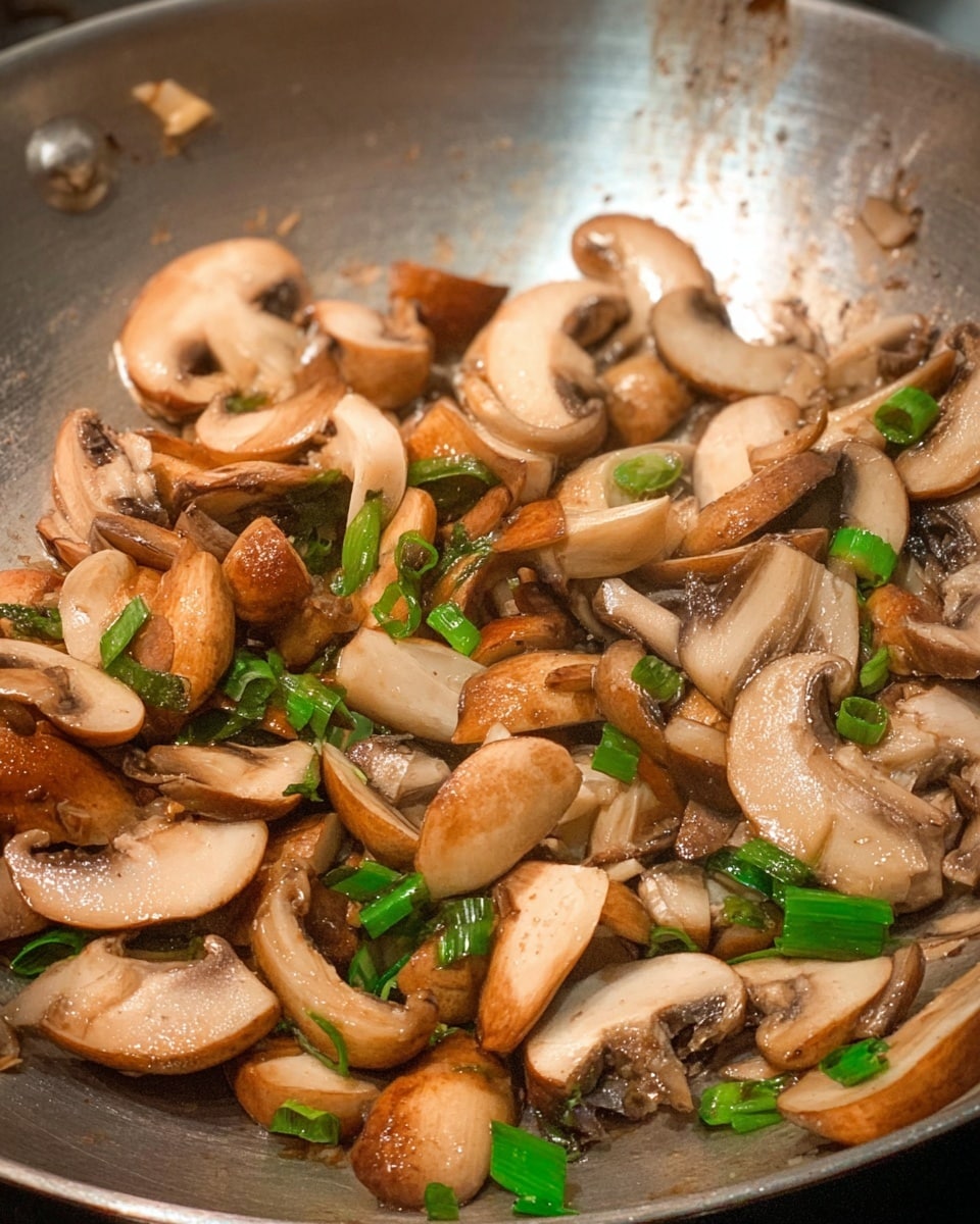 The image shows many pieces of cooked mushrooms in a metal pan, mixed with small pieces of green onions. The mushrooms are light to dark brown with a soft texture, some showing gills on the underside. The green onions add small, bright green color bits scattered evenly through the mushrooms. The shiny metal pan has some cooking oil reflections on its surface. The photo is taken with an iphone --ar 4:5 --v 7