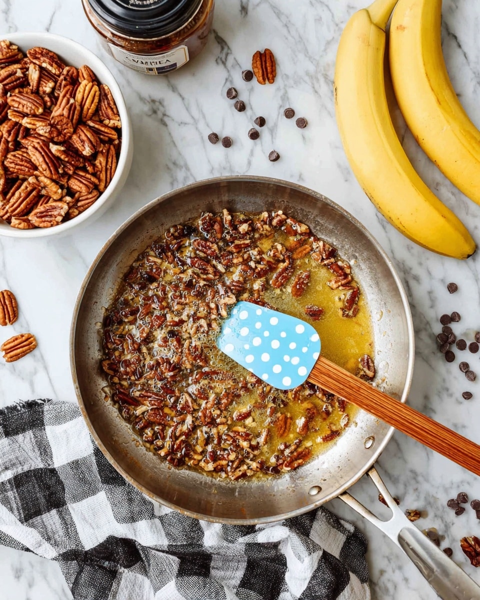 A metal pan filled with a layer of chopped pecans soaked in a golden, bubbling liquid, with a blue spatula with white polka dots and a wooden handle resting in the pan’s center. To the left, there is a white bowl full of whole pecans. Two ripe yellow bananas with brown spots lie in the upper right corner, near scattered dark chocolate chips. The setup is on a white marbled surface with a black and white checkered cloth partially under the pan. A jar with a black lid labeled vanilla is partially visible in the top left corner. Photo taken with an iphone --ar 4:5 --v 7