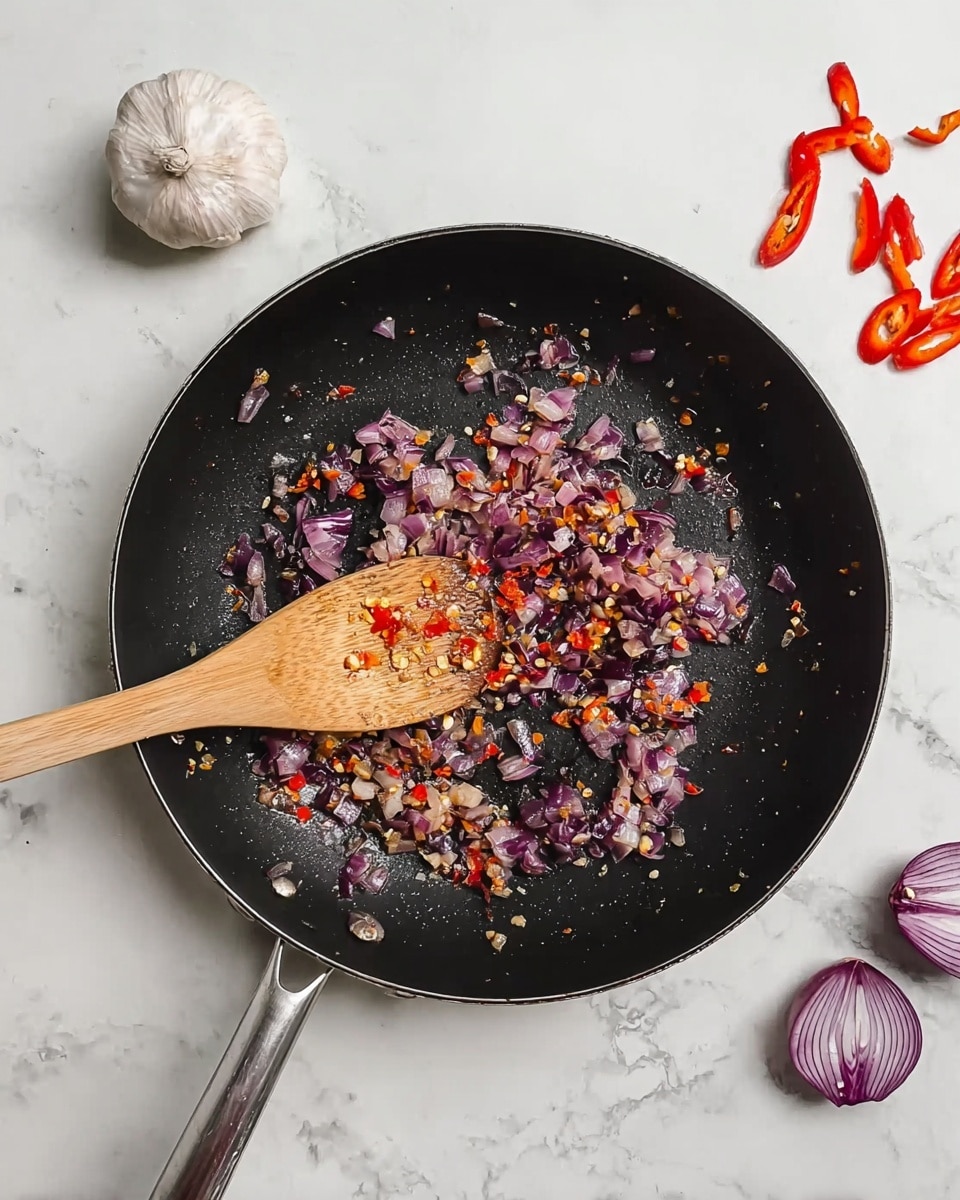 A black pan contains small pieces of cooked onion and red chili scattered in the center, with a wooden spoon resting inside the pan over the mix. Around the pan on a white marbled surface, there is a whole garlic bulb in the top left corner, two red peppers and one halved red onion on the bottom right. The pan has a metal handle visible on the left side. The onions are purple and translucent with bits of bright red chili pepper pieces mixed in, showing a cooked texture. Photo taken with an iphone --ar 4:5 --v 7