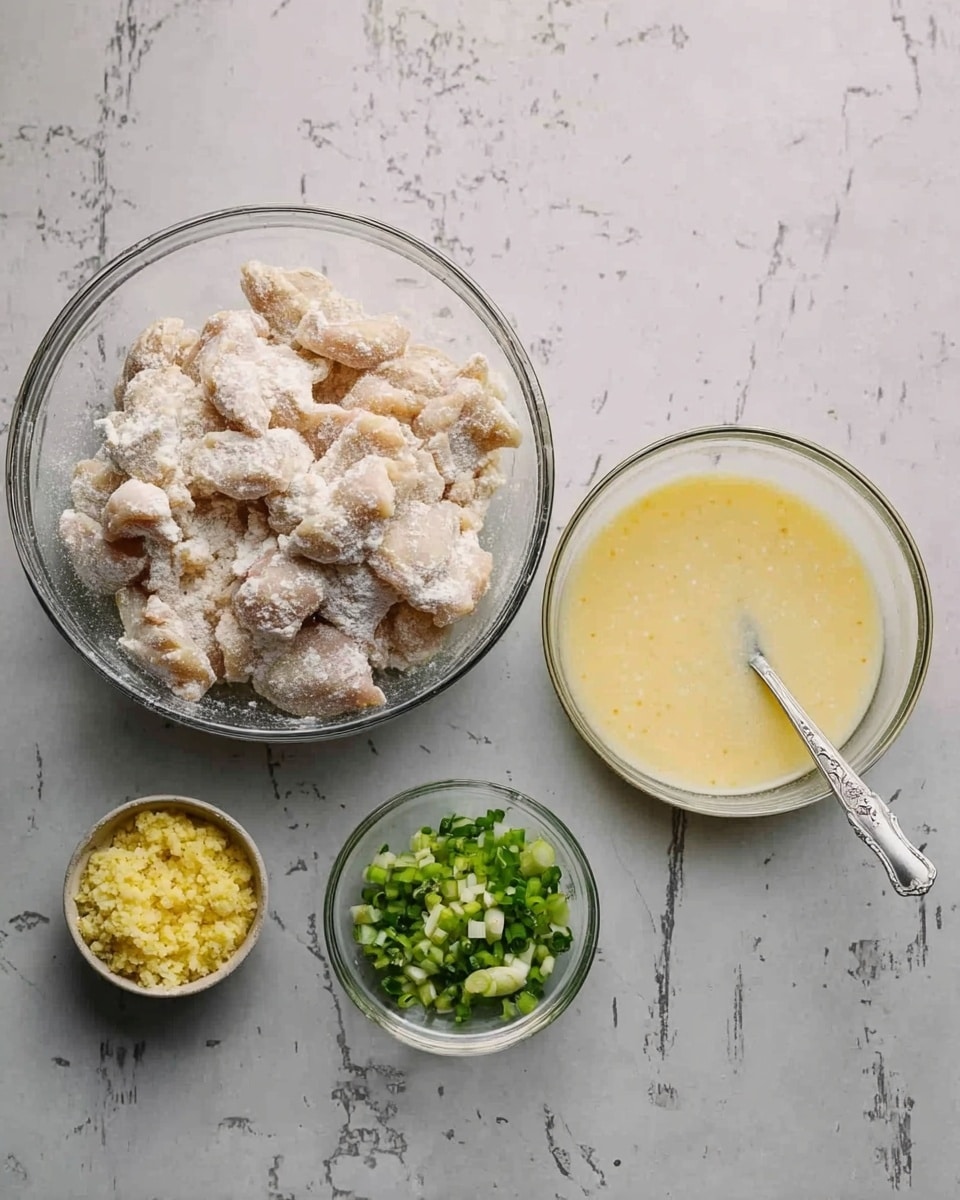 The image shows three clear glass bowls on a white marbled surface. The largest bowl on the left is filled with raw chicken coated in a white powdery mixture. To the right is a medium bowl with a pale, creamy yellow liquid and a spoon resting inside it. Below the large bowl are two small bowls, one containing minced yellow garlic and the other filled with chopped green onions. The textures contrast from the powdery chicken coating, smooth liquid, to the minced and chopped ingredients in the smaller bowls. Photo taken with an iphone --ar 4:5 --v 7