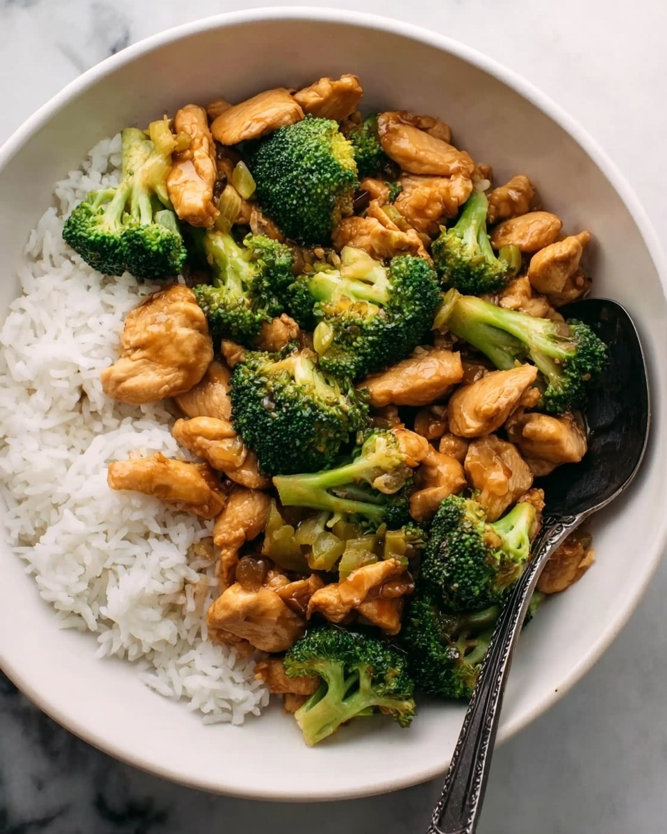 A white bowl filled with a layer of plain white rice at the bottom. On top, there is a mix of golden brown cooked chicken pieces and bright green broccoli florets, all coated in a slightly shiny sauce. The chicken pieces are unevenly shaped and the broccoli looks fresh and crisp. A dark silver spoon rests on the side inside the bowl. The bowl is placed on a white marbled surface. Photo taken with an iphone --ar 4:5 --v 7