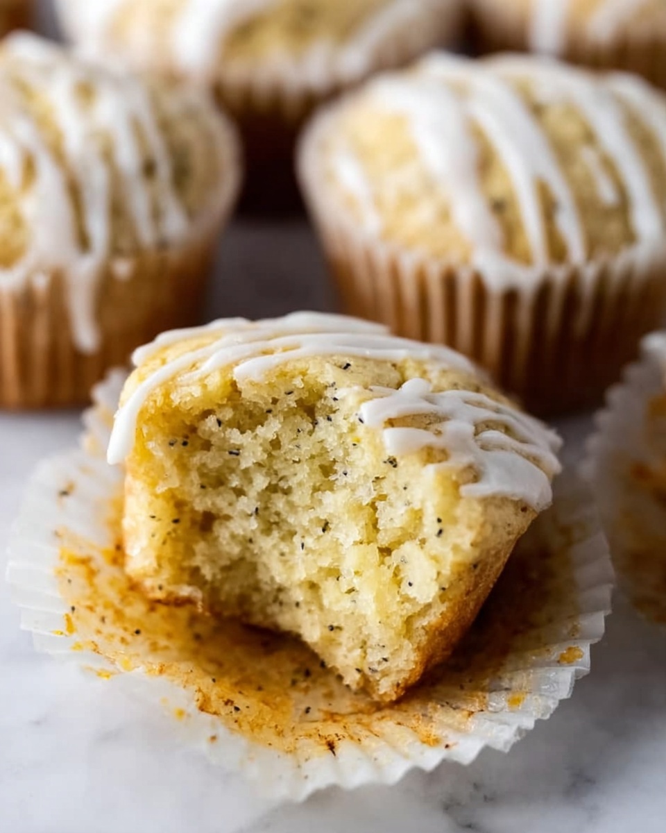 A close-up view of a small muffin with a bite taken out of it, showing its soft, light yellow inside with small black specks throughout. The muffin is topped with thin white icing stripes and sits in a crinkled white paper cup. Around it, there are more muffins with similar white icing on their tops, all placed on a white marbled surface. Photo taken with an iphone --ar 4:5 --v 7