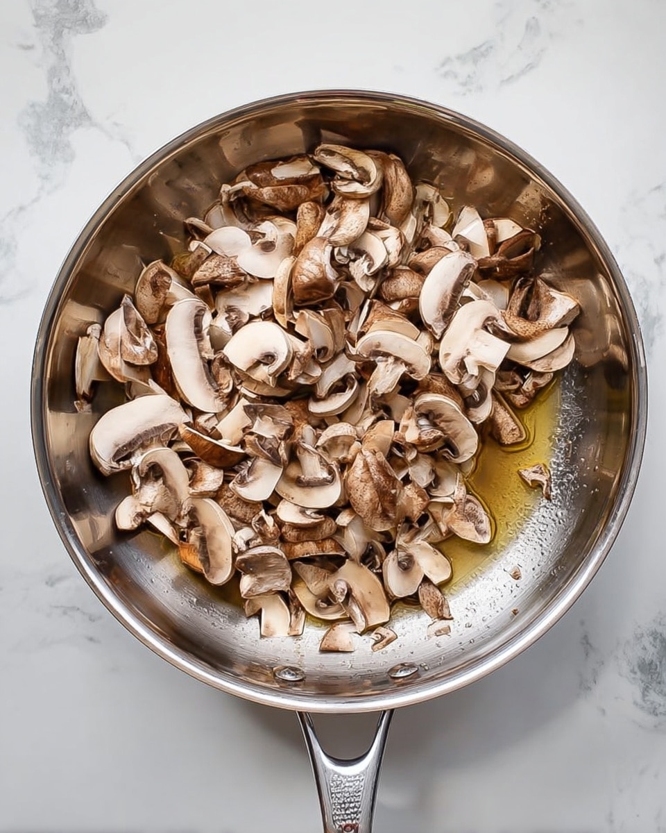 A shiny silver frying pan filled with many pieces of sliced brown mushrooms, some of the slices show the white inside and layers of the mushrooms, all sitting on a small amount of clear cooking oil at the bottom of the pan, placed on a white marbled surface. photo taken with an iphone --ar 4:5 --v 7