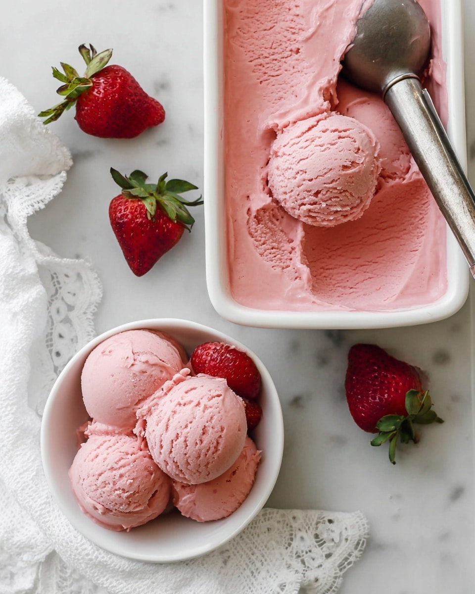 There is a white rectangular dish filled with smooth, creamy pink strawberry ice cream, with a metal scooper resting inside on the right. Below and centered, a white bowl holds four round scoops of the same pink ice cream, some with a soft texture and slight melting. A silver spoon rests inside the bowl on the right side. Two fresh strawberries with green leaves lie on the white marbled surface to the left of the bowl. A white cloth with lace detail is placed to the right near the bowl. Photo taken with an iphone --ar 4:5 --v 7