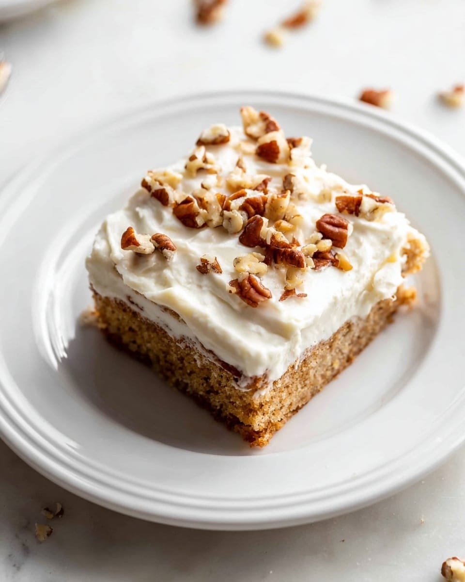 A square piece of cake is shown on a white plate with a simple edge design. The cake has two layers: the bottom layer is light brown with a soft texture, and the top layer is thick white cream frosting, smooth but with some swirls. On top of the frosting, there are small pieces of chopped pecans scattered unevenly. The plate sits on a white marbled surface with a few stray nut pieces around. photo taken with an iphone --ar 4:5 --v 7