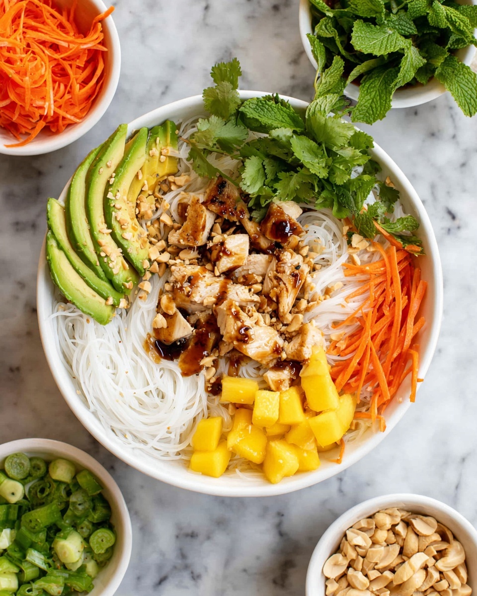 A white bowl holds a vibrant, layered dish. The bottom layer is white rice noodles, soft and slightly tangled. On top, there is grilled chicken, cut into small pieces with a light brown grilled texture, drizzled with a tan sauce and sprinkled with crushed peanuts. Around the chicken, fresh green cilantro leaves sit in the center. To the left, thinly sliced avocado fanned out in light green layers with black pepper and a dark soy sauce pool in the middle. Next to the avocado, small yellow mango cubes add a bright pop of color. Shredded orange carrots are placed near the mango and continue around the bowl. On the right side, more rice noodles with sprinkled crushed peanuts appear. Close by, chopped green onions and additional mango cubes add texture and color. Fresh mint leaves garnish the dish near the mango and avocado. Surrounding the bowl are small white dishes filled with shredded carrots, crushed peanuts, and sliced green onions, all set on a white marbled surface. Photo taken with an iphone --ar 4:5 --v 7
