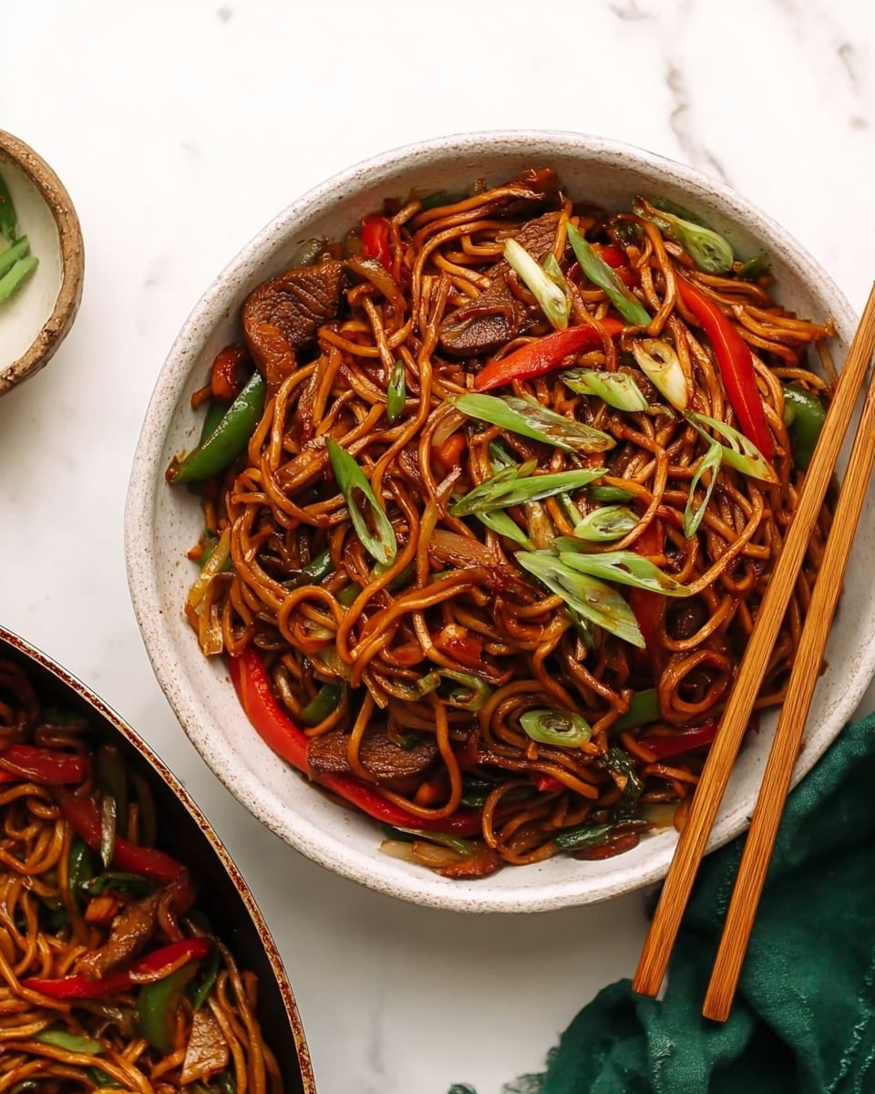 A bowl filled with stir-fried noodles, layered with dark brown glossy noodles covering most of the bowl, mixed with bright red and green sliced vegetables scattered throughout. Pieces of cooked meat are mixed in, showing some brown caramelized edges. Thin, fresh green onion slices are sprinkled on top, adding a fresh touch. Wooden chopsticks rest on the right side of the bowl, angled diagonally over the noodles. The bowl is white with a rustic texture inside, placed on a white marbled surface with a green cloth visible in the top right corner. Part of a pan with more noodles and vegetables is seen on the left side. Photo taken with an iphone --ar 4:5 --v 7