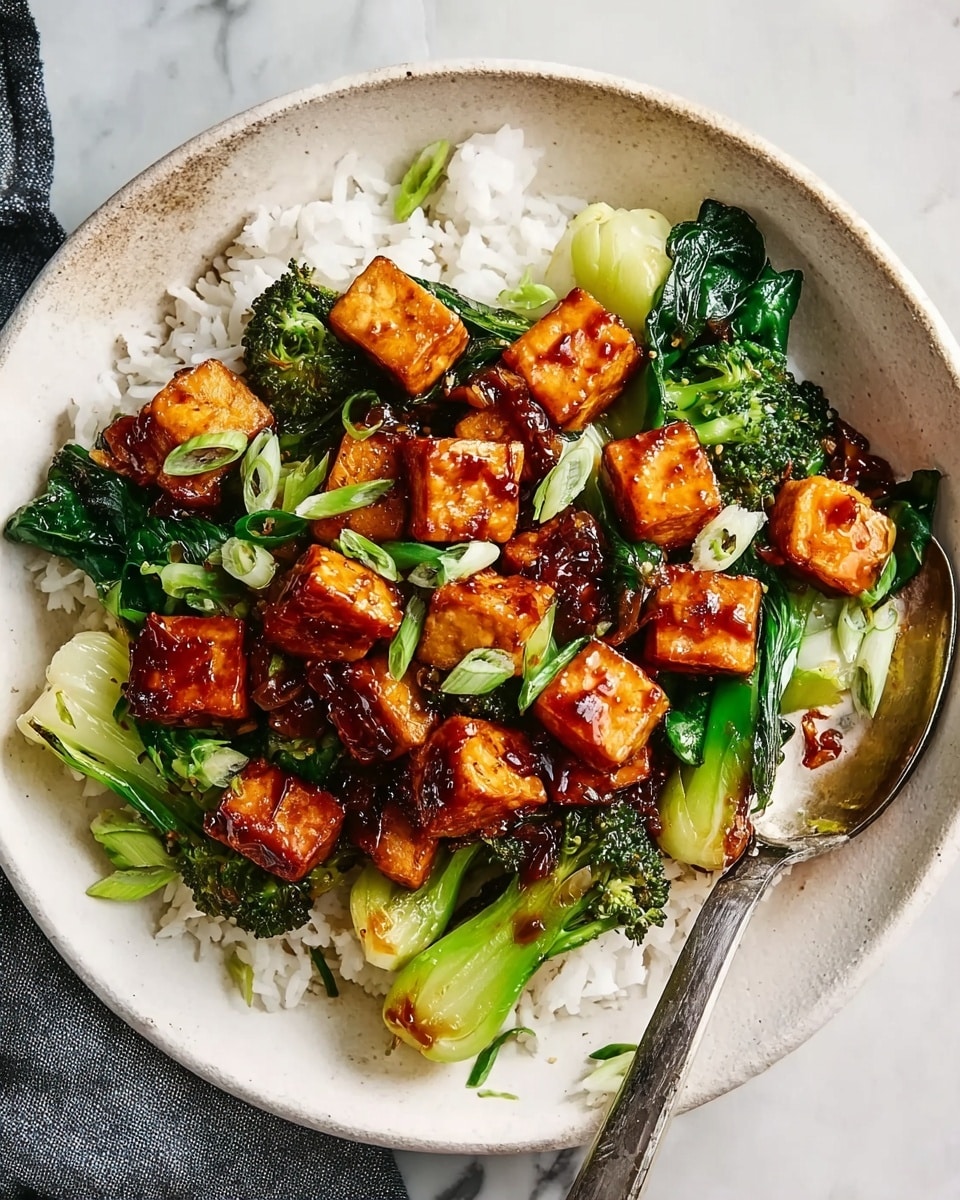 The dish shows a bowl filled with white rice as the base layer. On top of the rice, there are small cubes of golden-brown cooked tofu covered in a shiny, dark reddish sauce. Mixed with the tofu are bright green steamed vegetables like broccoli, baby bok choy, and scallions adding freshness and texture. The bowl is round and white, placed on a white marbled surface with a silver spoon resting on the side. The colors are vibrant with the warm tones of the tofu contrasting the fresh greens and pure white rice. photo taken with an iphone --ar 4:5 --v 7