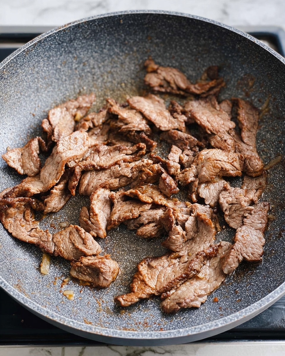 Thin slices of light brown cooked meat with some darker brown seared edges are spread unevenly in a speckled gray pan. The pan sits on a black stove grate under soft natural light. Thin layers of meat overlap slightly in places, showing varied texture from smooth to wrinkled. The pan surface looks clean with some small spots of oil and juice from cooking. The background has a white marbled texture. Photo taken with an iphone --ar 4:5 --v 7