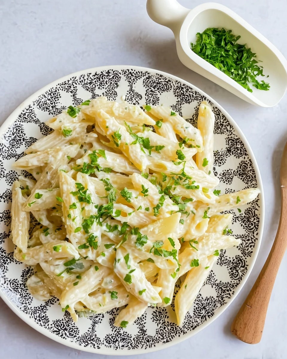 A white round plate with a black decorative pattern holds one layer of creamy penne pasta. The pasta is coated in a smooth white sauce and is sprinkled with small pieces of green parsley scattered evenly on top. To the upper right side, a white wooden scoop filled with chopped green herbs rests on a white marbled surface. The overall scene is bright and clean with a simple but fresh look. photo taken with an iphone --ar 4:5 --v 7